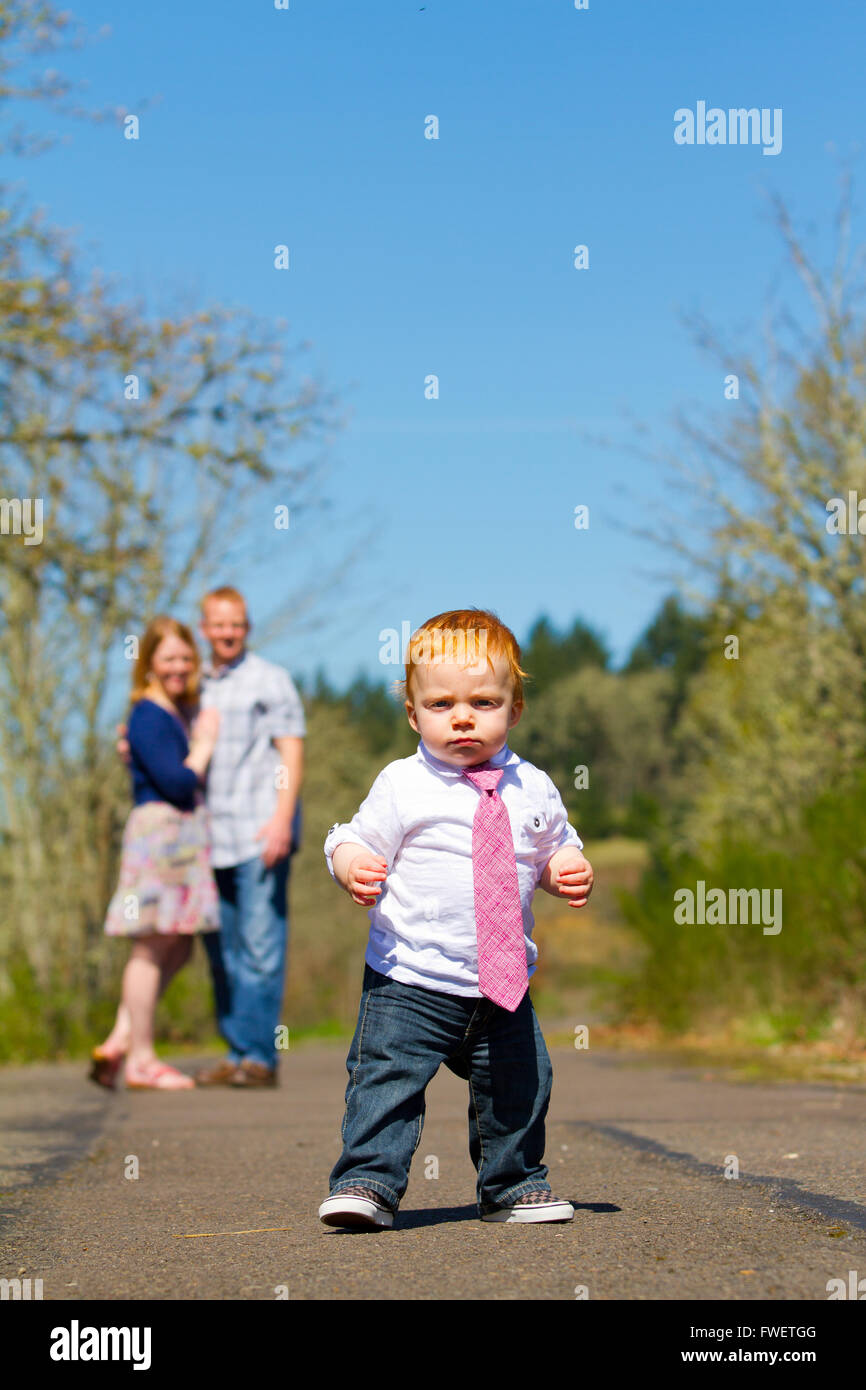 Parents are out of focus in this selective focus image while a baby boy runs toward the camera. Stock Photo