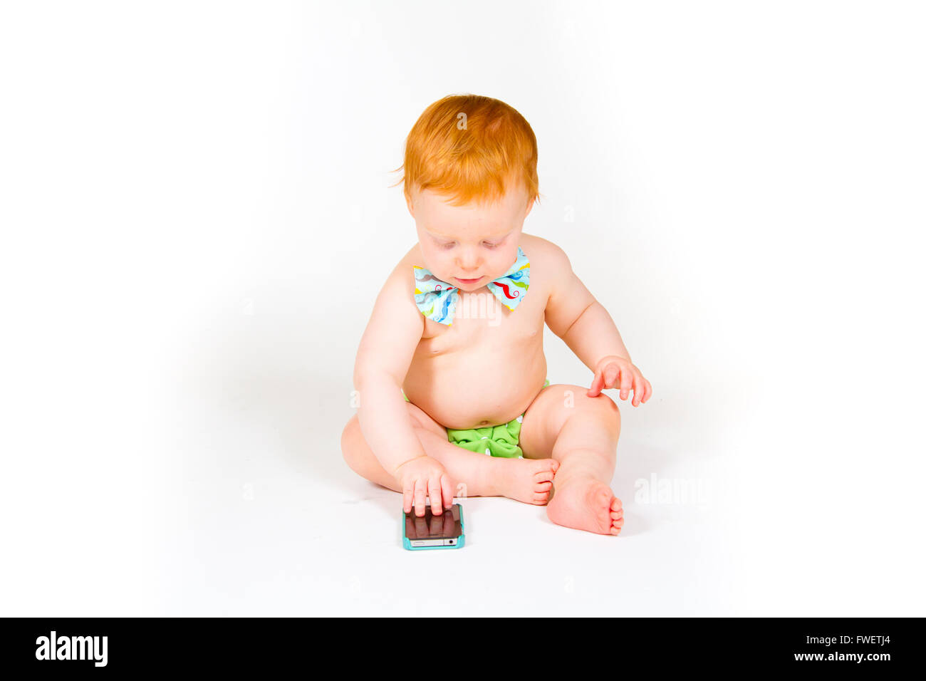 A one year old boy plays with a cell phone in the studio with a white background. Stock Photo
