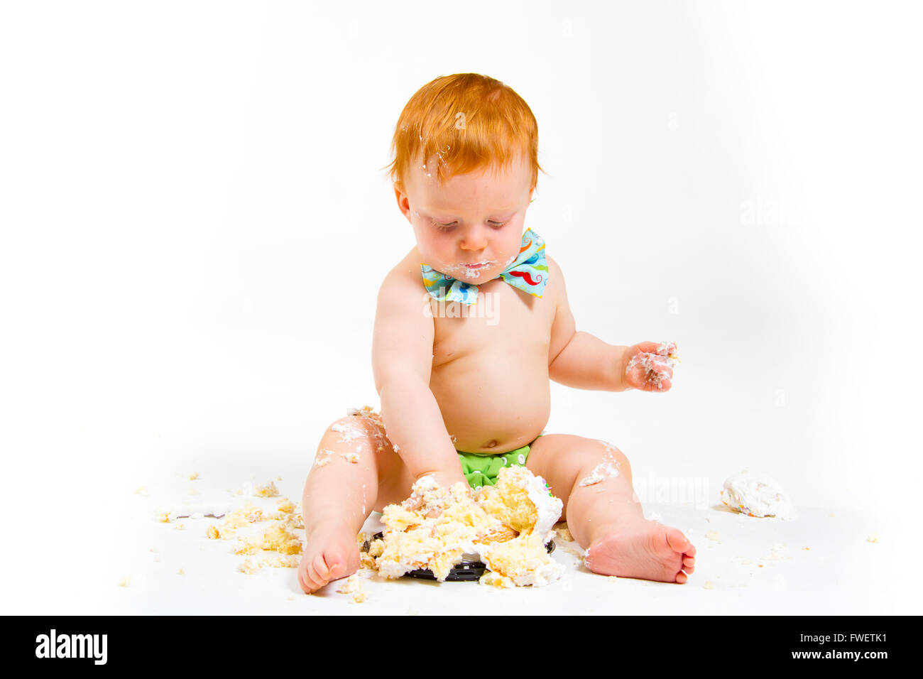 A baby boy gets to eat cake for the first time on his first birthday in this cake smash in studio against a white background. Stock Photo