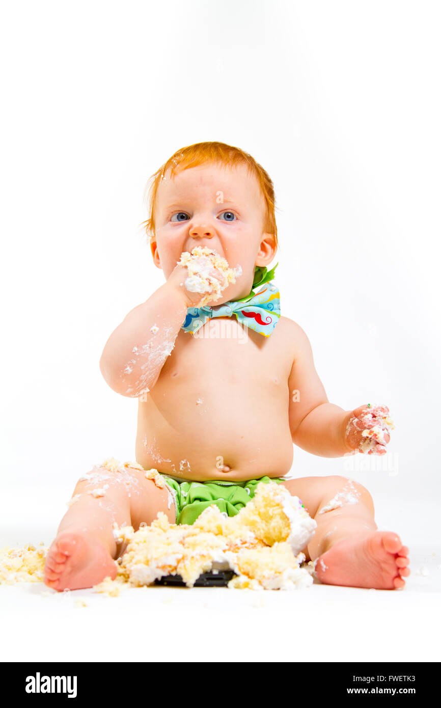 A baby boy gets to eat cake for the first time on his first birthday in this cake smash in studio against a white background. Stock Photo