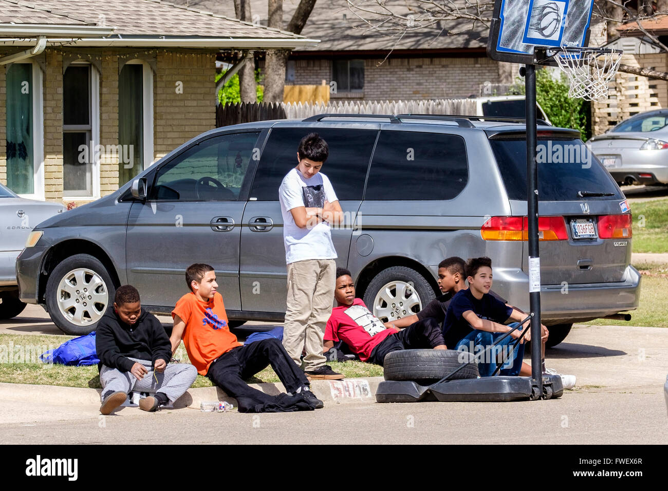 Six preteen boys take a break from playing basketball and sit on a neighborhood curb together in Oklahoma City, Oklahoma, USA. A Stock Photo