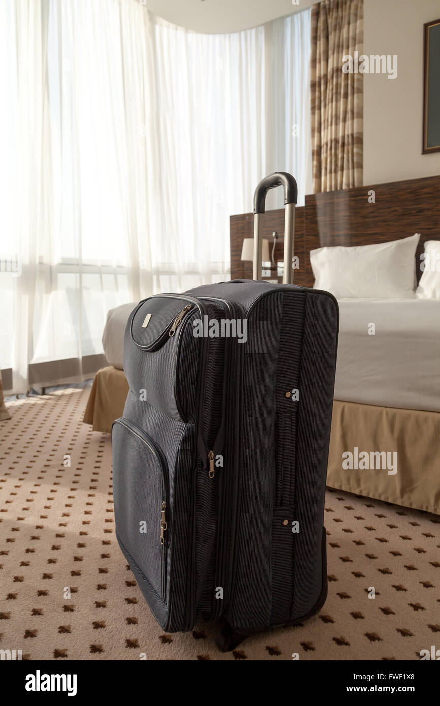 Large blue wheeled suitcase standing on the floor in the hotel room. Vertical image Stock Photo