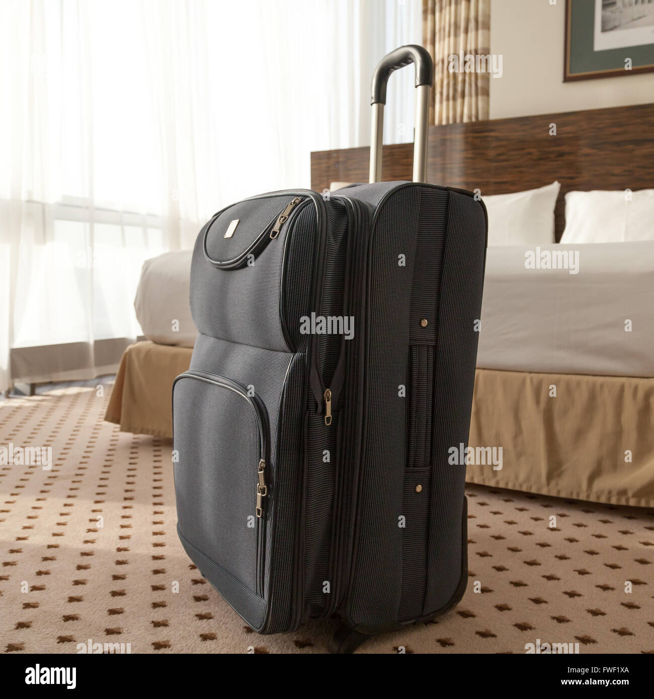 Large blue wheeled suitcase standing on the floor in the hotel room. Travel lifestyle concept. Square image Stock Photo