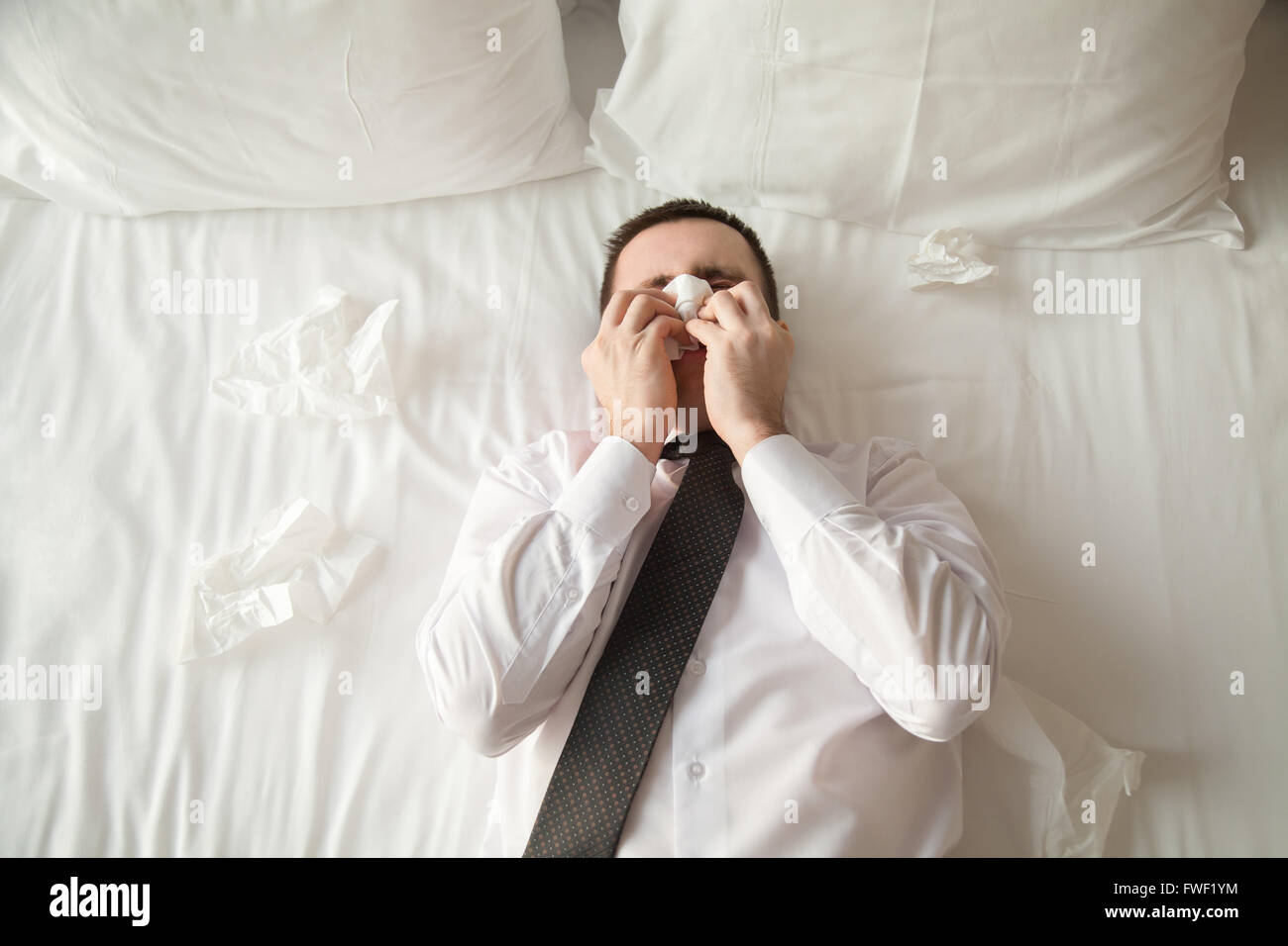 Portrait of young businessman wearing white shirt and necktie lying on the bed in the hotel room sick with flu Stock Photo