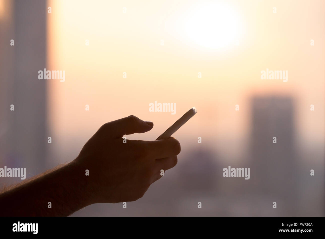 Close-up of hands of young man holding mobile phone, using smartphone app, scrolling. silhouette against sunny street view Stock Photo