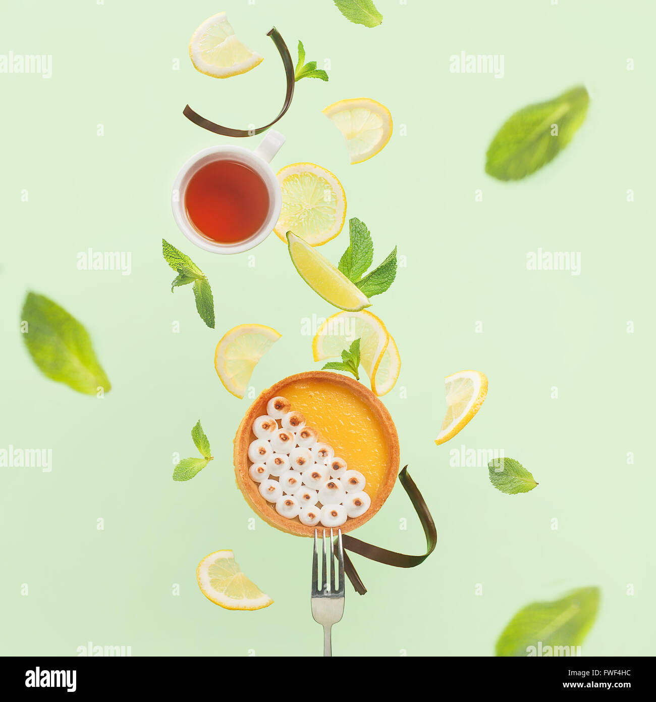 Lemon tart with cup of tea, lemon slices and mint leaves, balancing on a fork Stock Photo