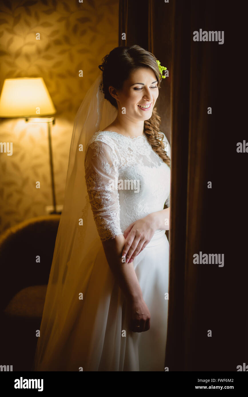bride in a white dress standing near window Stock Photo - Alamy