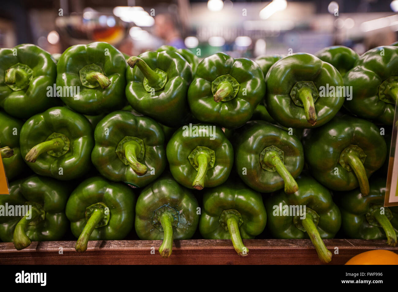 a tightly packed stack of green bell peppers on display in the produce section of a grocery store Stock Photo