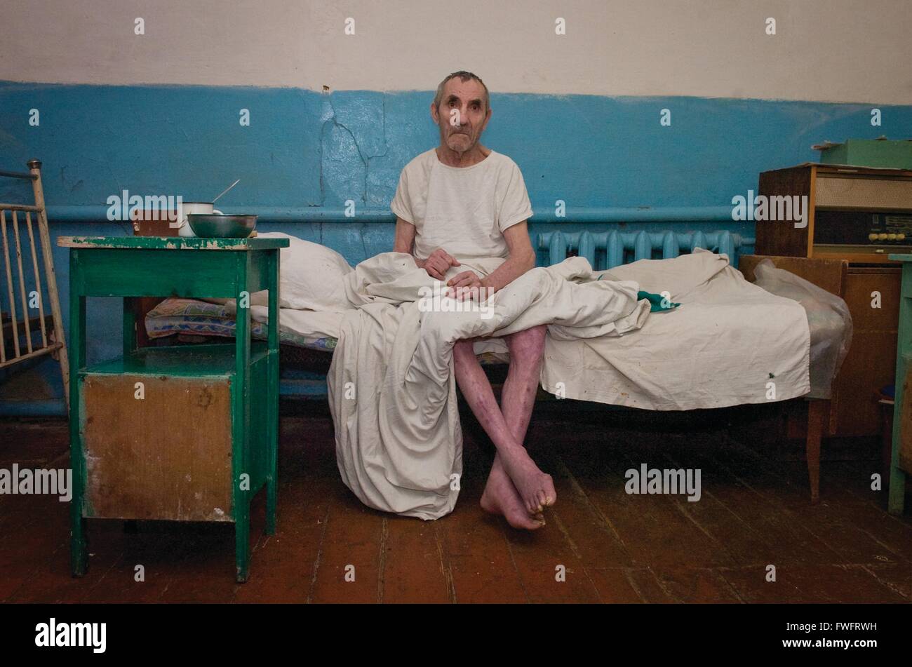 Didivschyna, Ukraine. An elderly resident of a government care home sits on his bed wearing a white shirt. The care home is run down and shabby and waiting for refurbishment by British Charity, International Aid Trust,based in Much Hoole, Preston, Lancashire Stock Photo