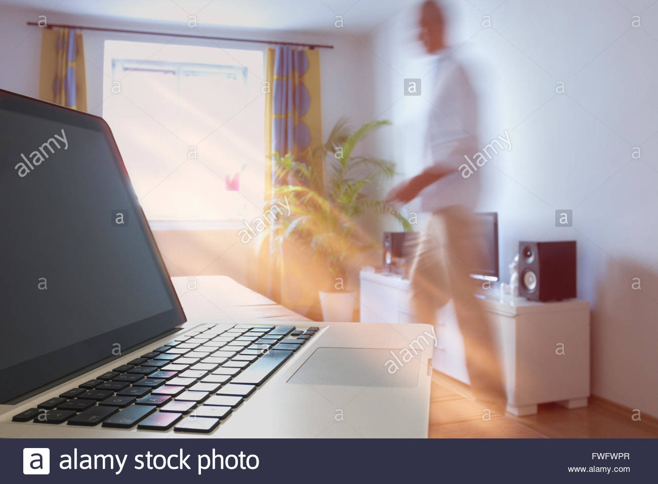 Laptop On Table With Man Walking In Background At Home Stock Photo