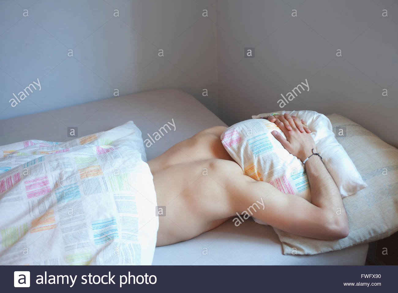 Young Man Sleeping With Head Under Pillow In Bed Stock Photo