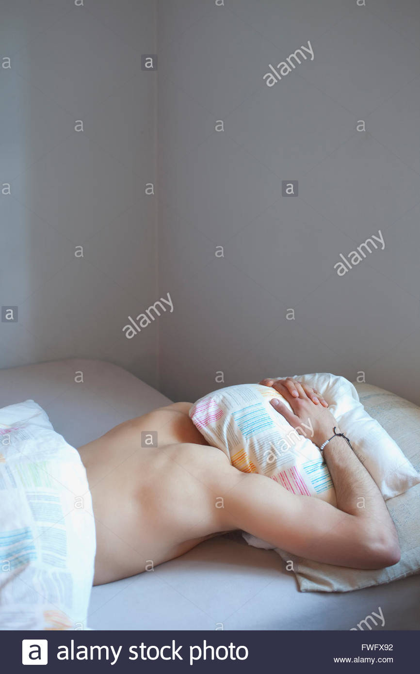 Young Man Sleeping With Head Under Pillow In Bed Stock Photo
