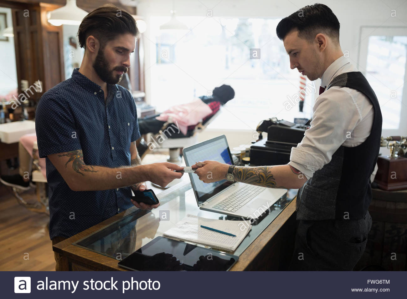 Man paying barber at counter in barber shop Stock Photo Alamy