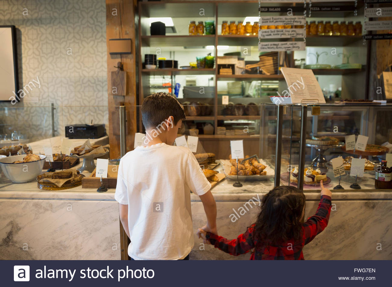 Brother and sister holding hands at bakery display case Stock Photo