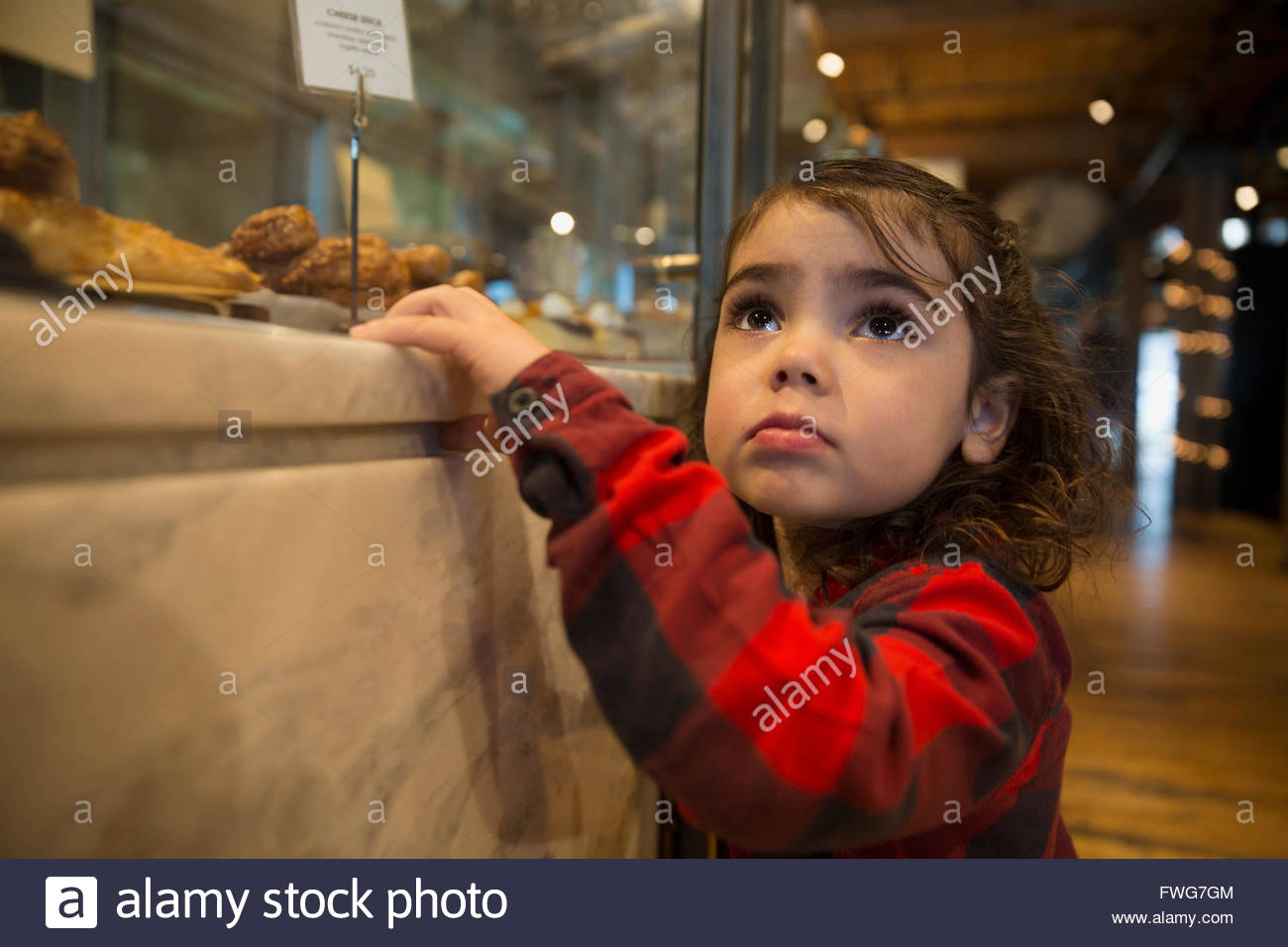 Cute girl looking up at bakery display case Stock Photo Alamy