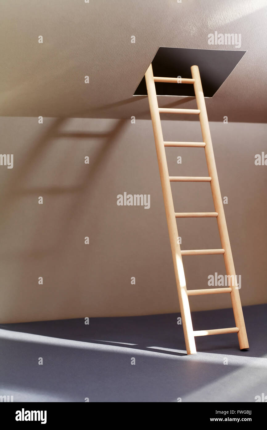 Escape concept. Wooden ladder in empty room with illuminated hatch in ceiling Stock Photo
