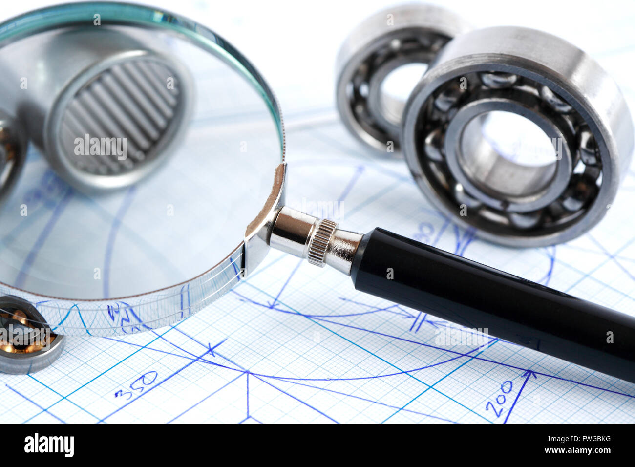 Engineering concept. Closeup of magnifying glass near ball bearings on blueprint with draft Stock Photo