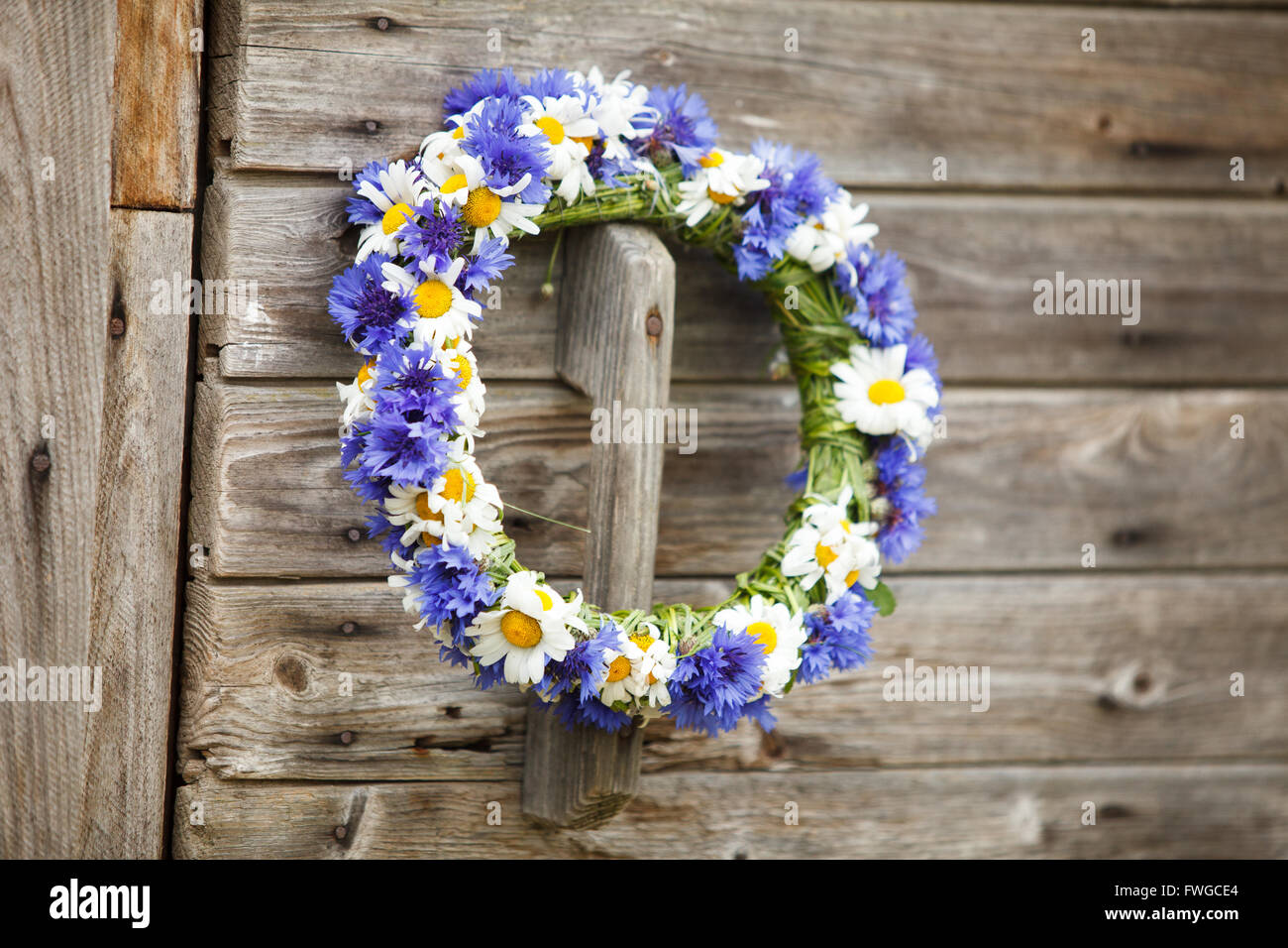 Chaplet from blue cornflowers on the wooden door Stock Photo