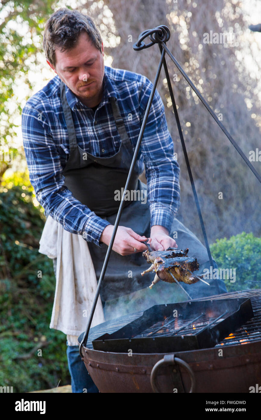 An outdoor cookout, a man lifted game birds off the griddle of an open fire. Stock Photo