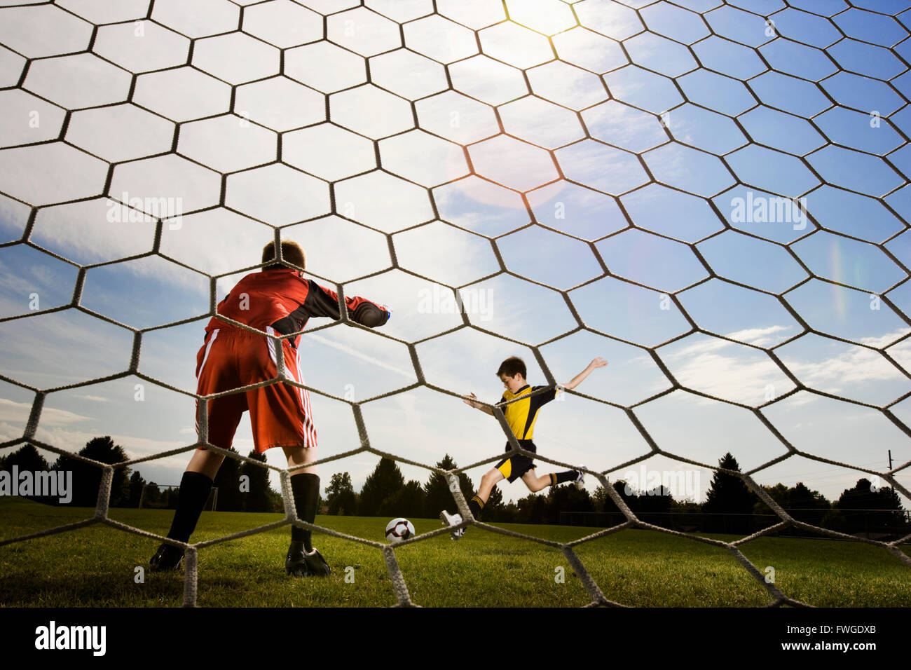 A soccer player taking aim and kicking at the goal, view from behind the goal keeper. Stock Photo