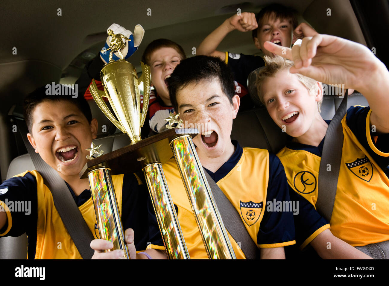 A group of boys in soccer team shirts holding a trophy and celebrating a win. In a team bus. Stock Photo