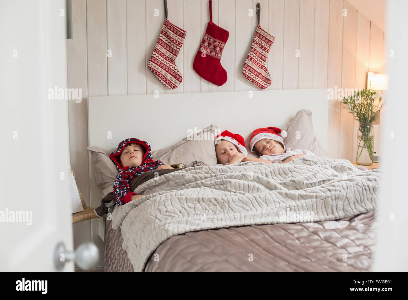 Three children in a double bed, with Christmas stockings hanging on the wall above their heads. Stock Photo