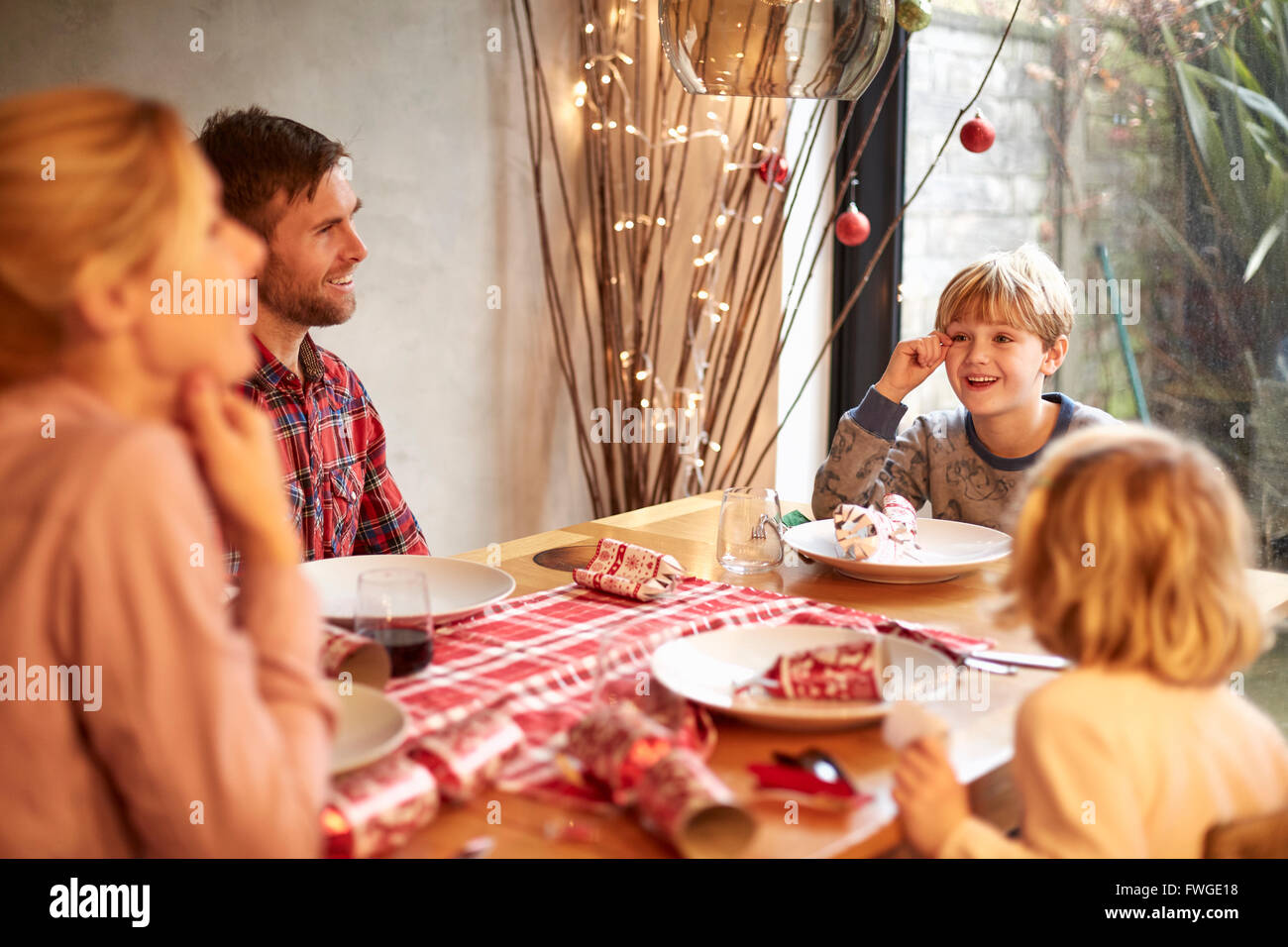 A family of four people, two adults and two children seated around  a table at Christmas time, pulling crackers. Stock Photo