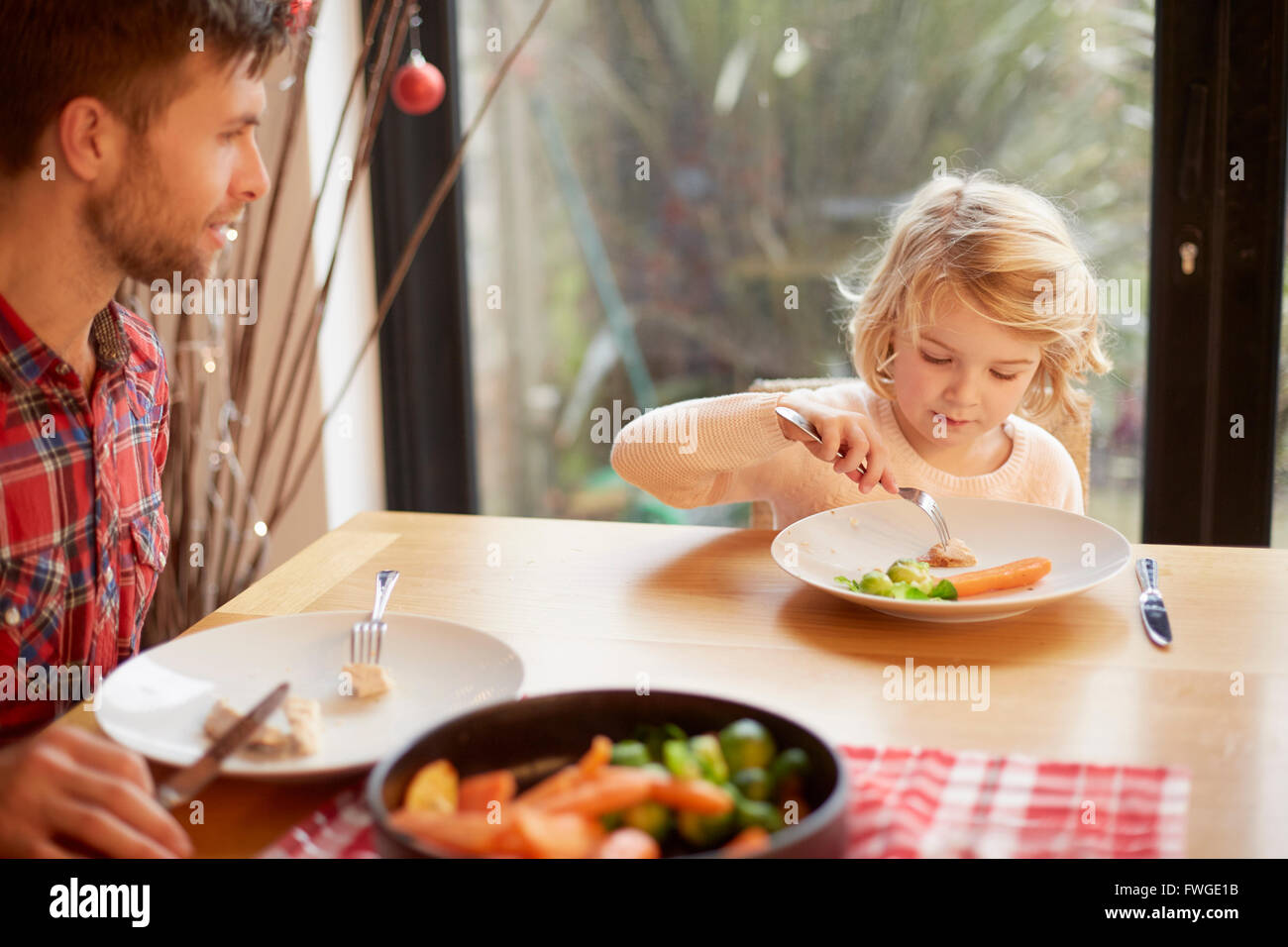 A child and a man sitting at a table eating a cooked meal. Stock Photo
