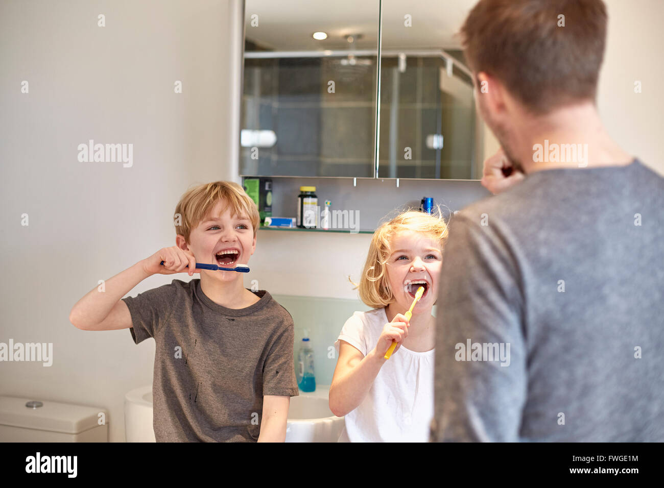 Two children and an adult man cleaning their teeth with toothbrushes in a bathroom. Stock Photo