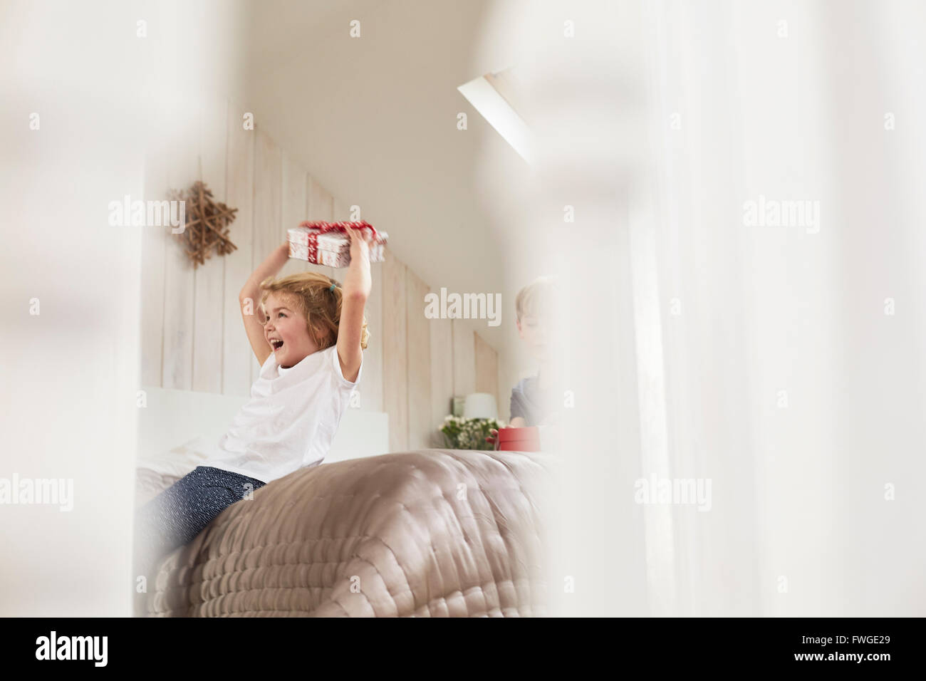 Christmas morning in a family home. A girl  holding a present above her head. Stock Photo