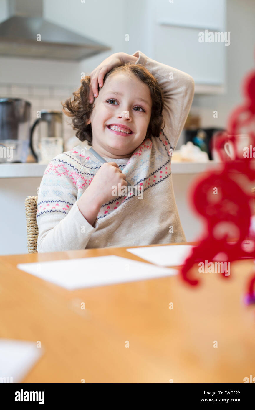 A child, a girl sitting at a table at home, drawing and writing cards before Christmas. Stock Photo