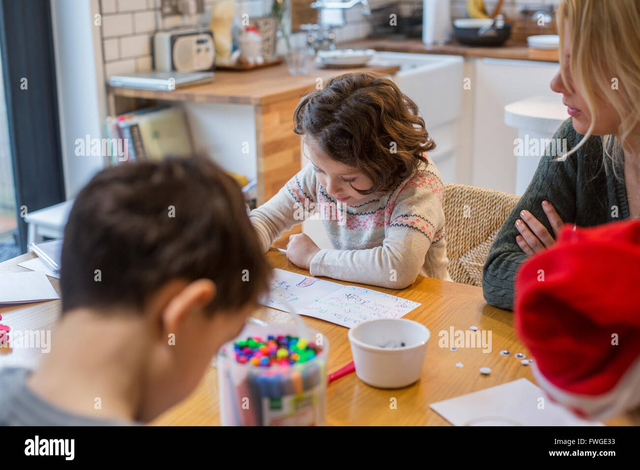 Three children and an adult woman at a table, drawing and writing cards and letters to Santa. Stock Photo