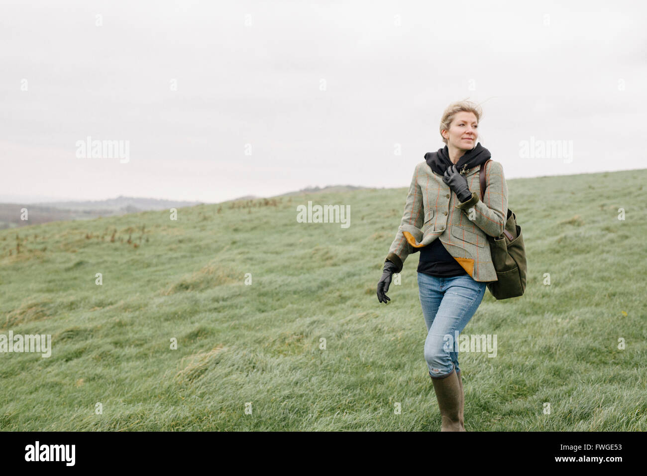 A woman in warm coat and gloves walking across open country, grassland and moors. Stock Photo