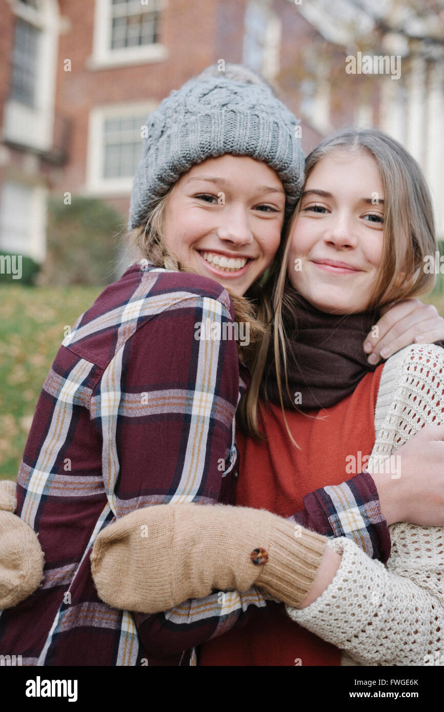 Two girls in hats and gloves wrapped up for cold weather, hugging and laughing. Stock Photo