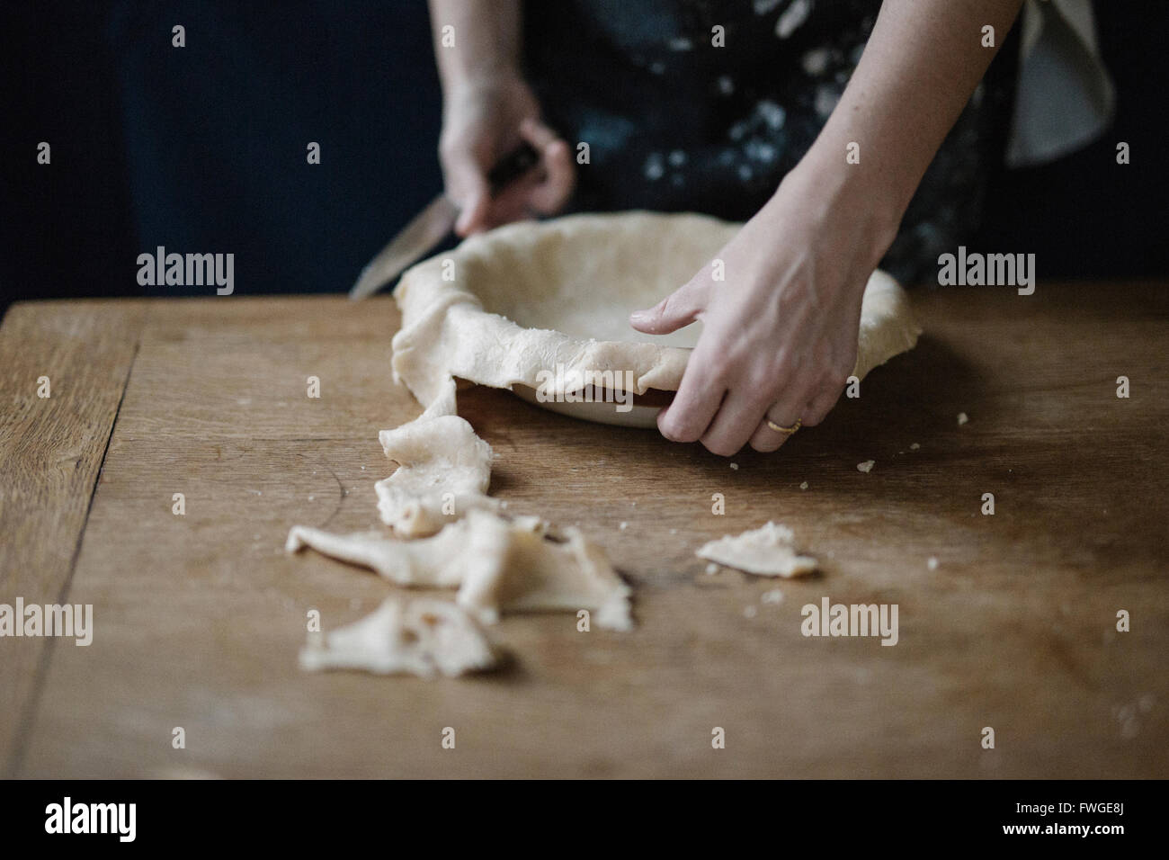 A woman using raw pastry dough to line a pie dish and finish the edge
