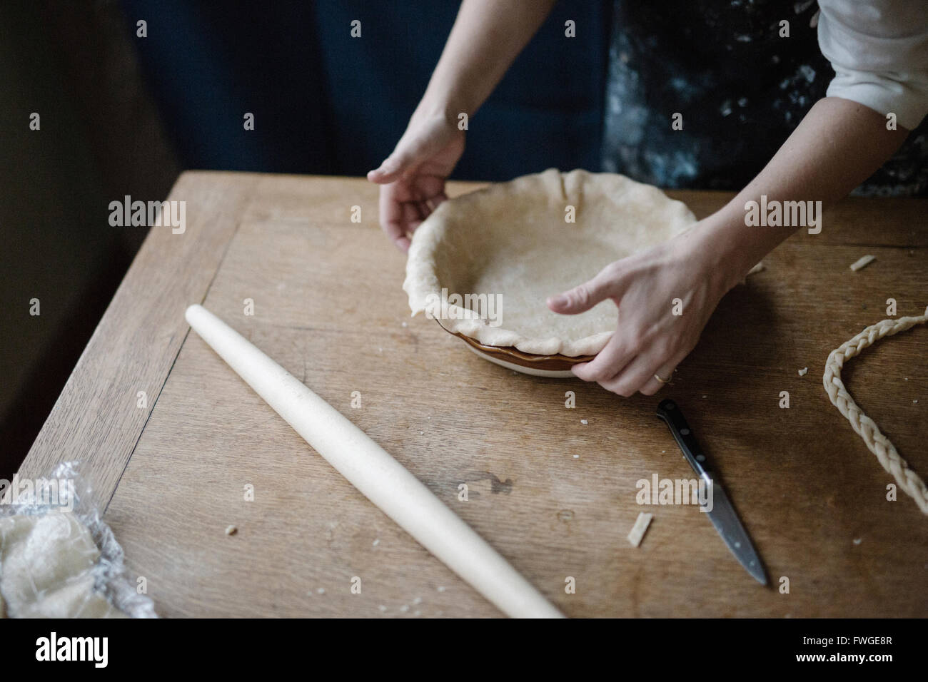 A woman working smoothing the edge of a pastry case lining a pie dish