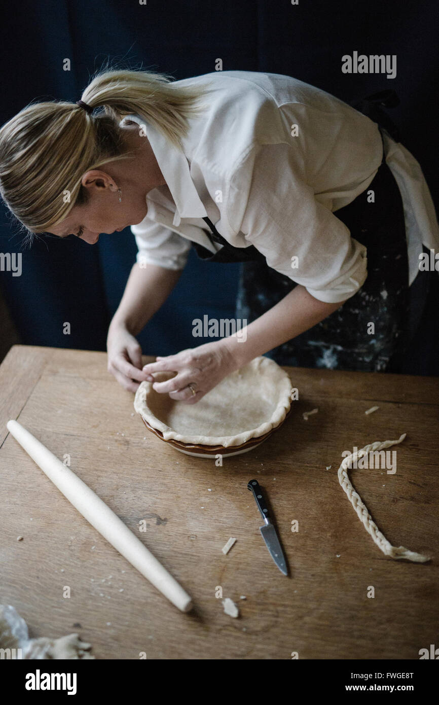 A woman working smoothing the edge of a pastry case lining a pie dish