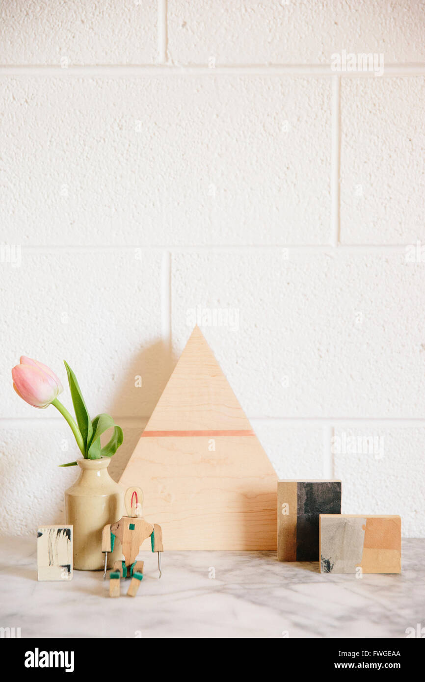 A stone worktop with a wooden triangle of wood, small cubes of wood and a pink tulip in a jar Stock Photo