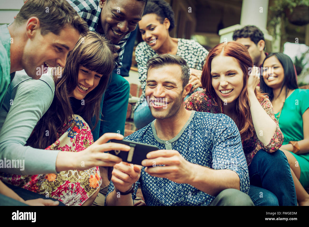 A group of friends on the steps of a house porch, looking at a smart phone selfy on the screen. Stock Photo