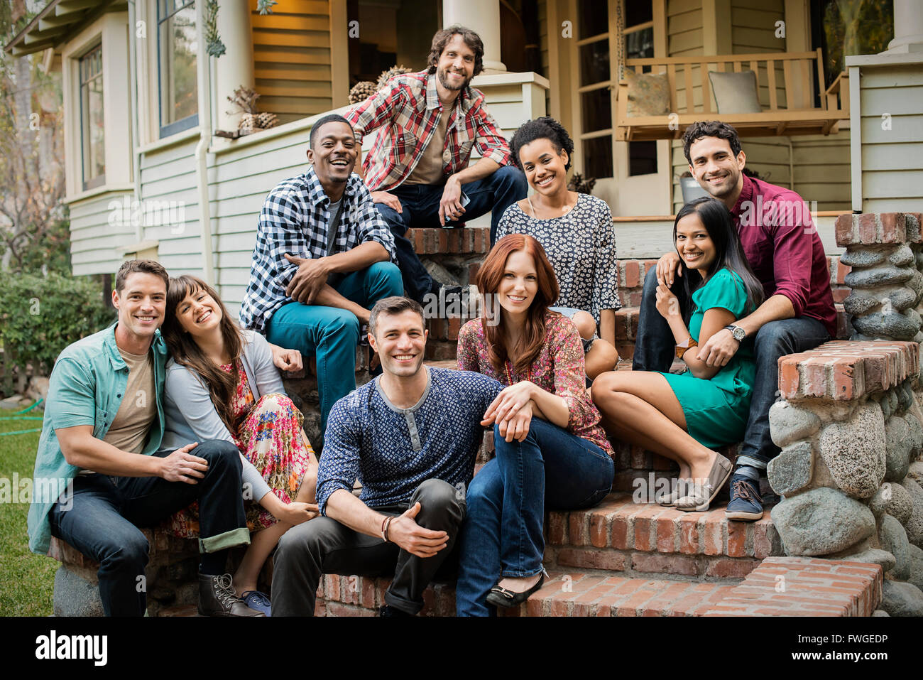 A group of friends sitting on the steps of a house porch, posing and laughing. Stock Photo