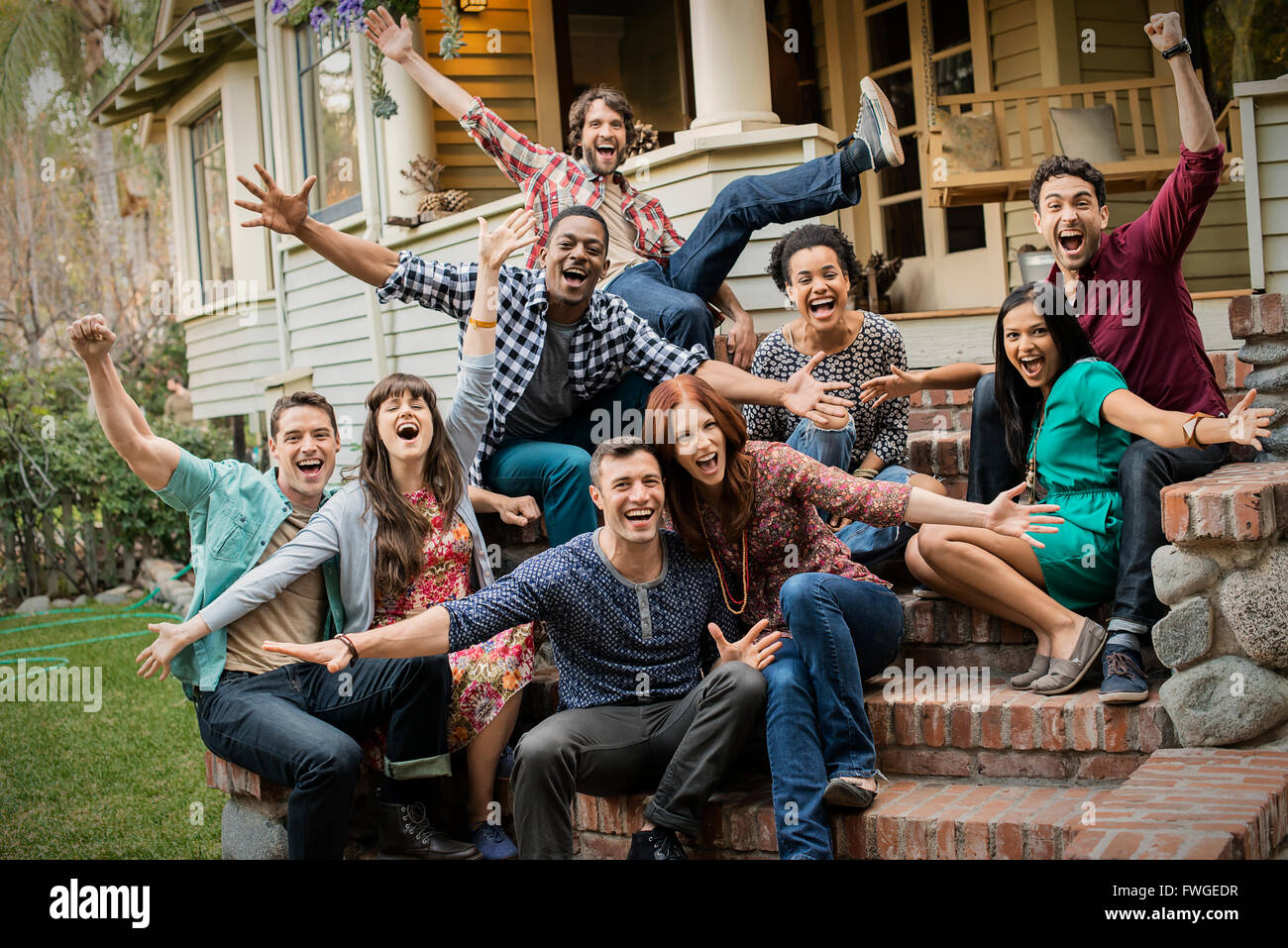 A group of friends sitting on the steps of a house porch, posing and laughing, arms outstretched. Stock Photo