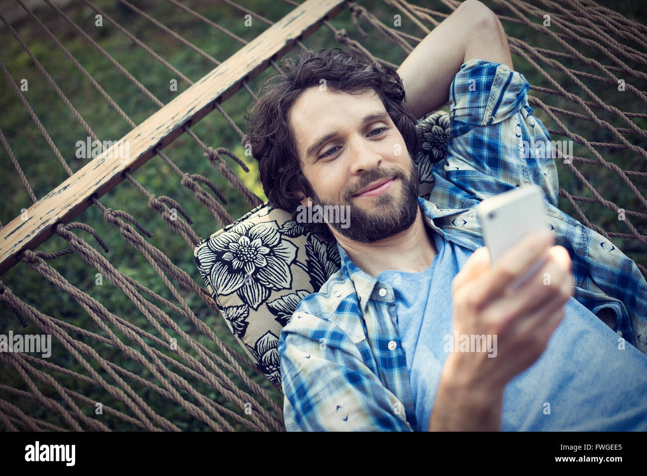 A man lying in a garden hammock taking selfies with his phone. Stock Photo
