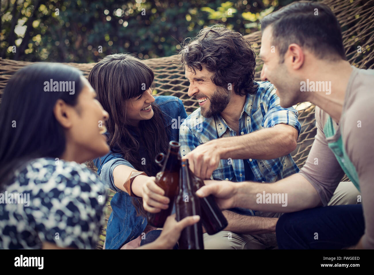 A group of friends lounging in a large hammock in the garden having a beer. Stock Photo