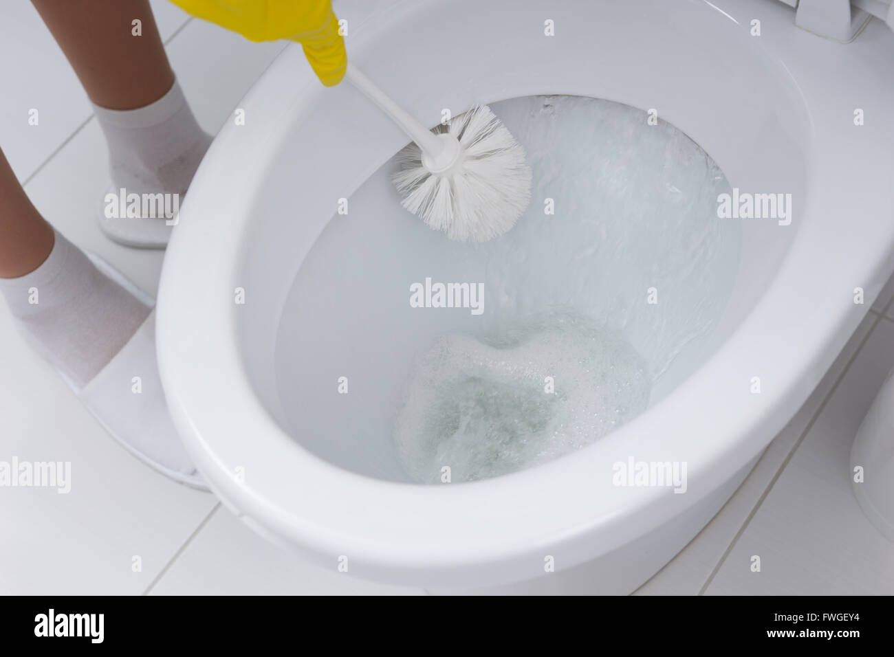 Housewife cleaning out the bowl of the toilet scrubbing under the rim with an antibacterial detergent and brush, close up of her hand. Stock Photo