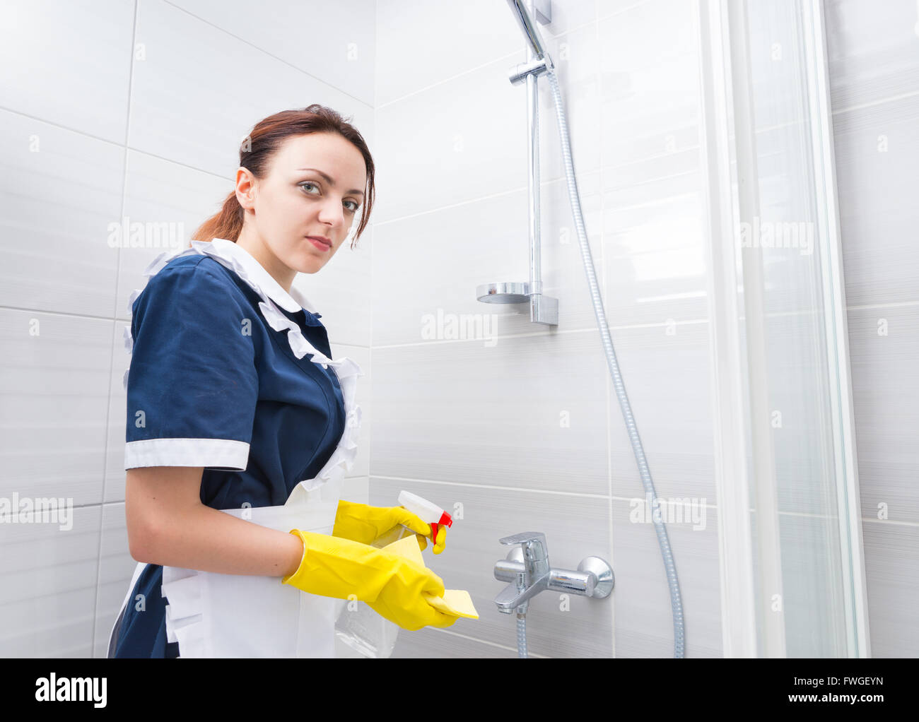 Housekeeper servicing a hotel bathroom standing inside the shower in