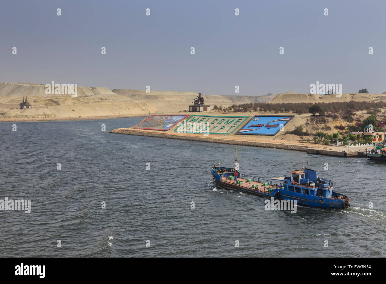 Small ship travels on the Suez Canal, past memorials and a large Welcome to Egypt sign, Ismalia, Egypt, North Africa Stock Photo
