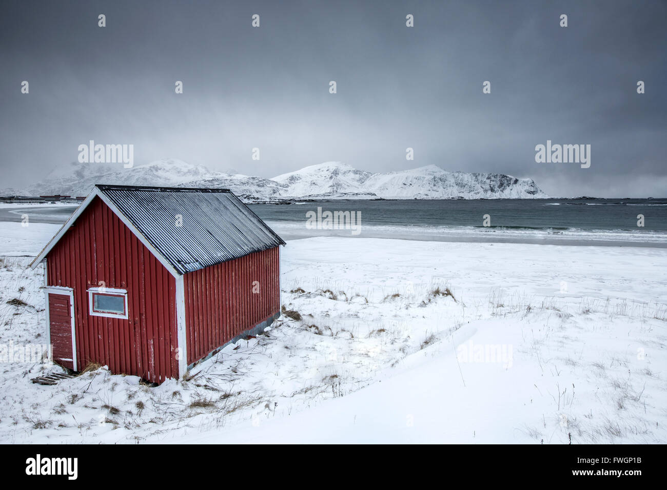 A typical house on the snowy beach frames the icy sea at Ramberg, Lofoten Islands, Arctic, Norway, Scandinavia Stock Photo