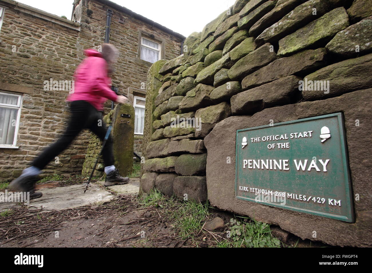 A female walker passes the sign marking the official start of the Pennine Way in Edale village, Peak District National Park, UK Stock Photo