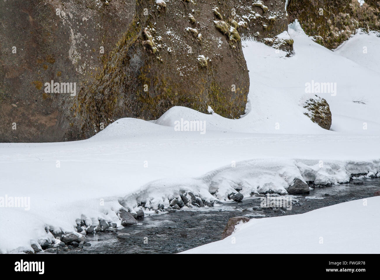Narrow stream between rocky cliffs, surrounded by snow.  Winter in Thorsmork, Iceland Stock Photo
