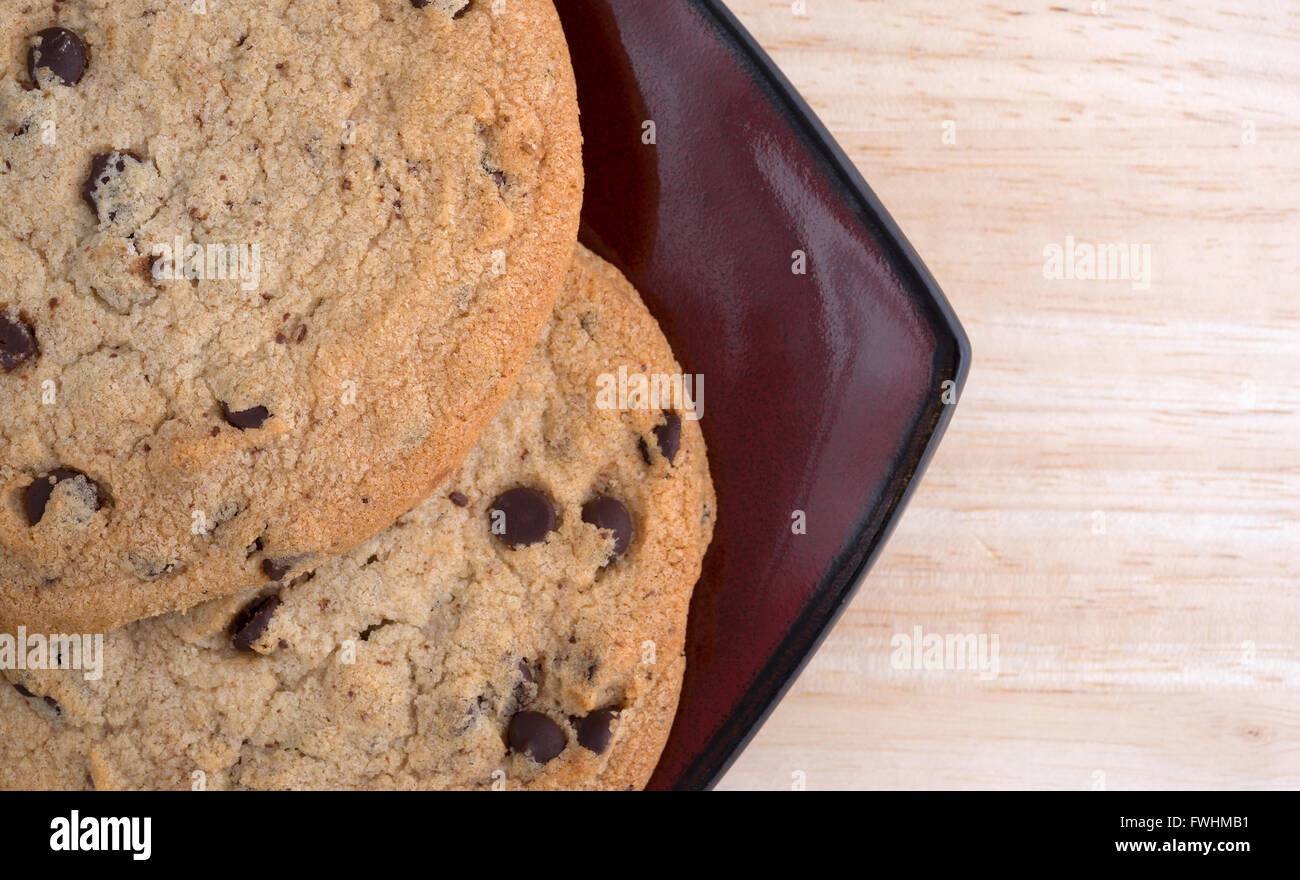 Top close view of two chocolate chip gluten-free cookies on a deep red plate atop a wood table top. Stock Photo